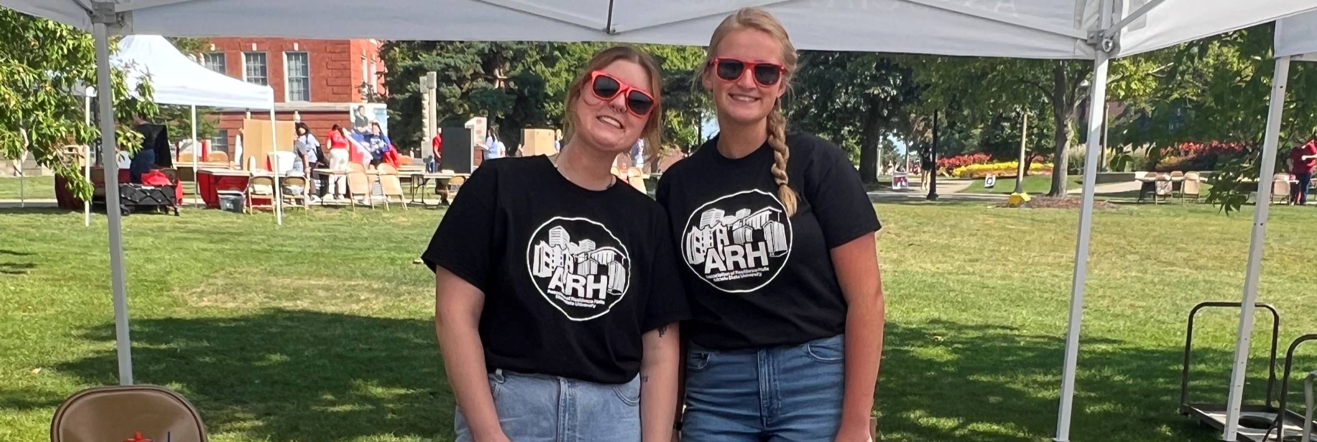 Two ARH members wearing matching black ARH t-shirts and red sunglasses represent ARH at Festival ISU.